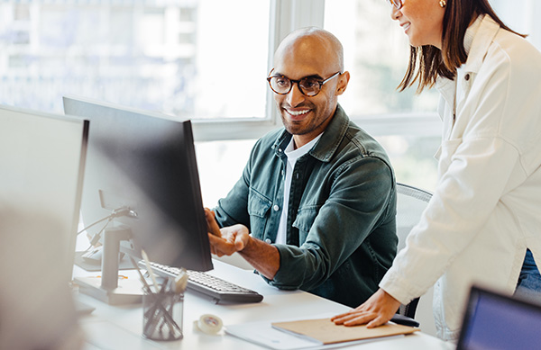 Two software engineers smiling and looking at a computer.