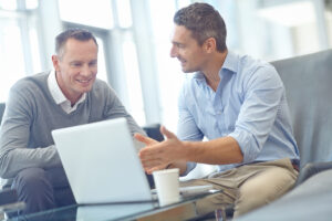 Two business men looking at a laptop and smiling.
