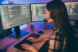 A woman typing on her computer with a headset on.