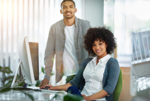 Two people sitting by a computer and smiling.
