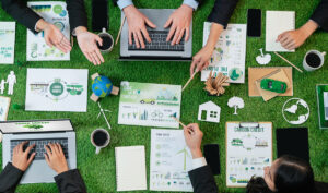Aerial view of a business table with people on laptops, phones, and papers about using green energy.